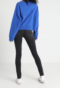 Przesadnie przerośnięty niebieski sweatshirt z długimi rękawami, czarne wąskie dżinsy i białe trampki. Gładka tekstura materiału, ściśnięte mankiety i pas.