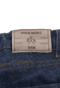 Farkut denim, joissa on beigetaustainen etiketti. Etiketissä lukee &quot;BAND OF RASCALS&quot; tummalla kirjoituksella, logon kanssa ja &quot;DENIM&quot; alapuolella. Tummansininen väri.