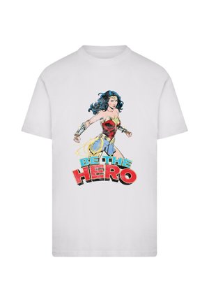 White cotton t-shirt featuring a comic-style illustration of a superhero in red and blue attire, with the text "BE THE HERO" in bold colors.