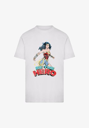 White cotton t-shirt featuring a comic-style illustration of a superhero in red and blue attire, with the text "BE THE HERO" in bold colors.