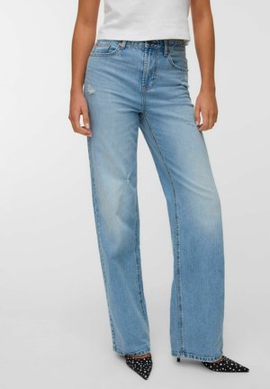 Woman wearing light blue high-waist straight-leg jeans with slight distressing, paired with black and white polka dot pointed heels and a white top.
