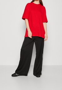 Červené oversized tričko s krátkým rukávem, spárované s volnými černými kalhotami s bílými bočními pruhy a černými teniskami. Jednoduchý design, pohodlný střih.