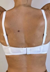 Sostén de algodón blanco con tirantes ajustables y cierre de gancho y ojal, con una textura suave y diseño sencillo. Vista trasera solamente.