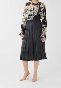 Jupe midi plissée noire associée à un blouse à motifs floraux en crème et noir, avec un tissu transparent et des manches évasées. Talons transparents en nude.
