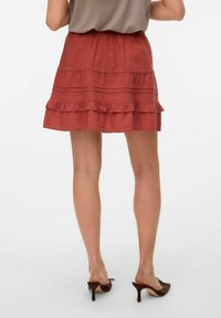 Falda roja en capas con dobladillo con volantes y rayas horizontales texturizadas. Cintura elástica. Se lleva con mule marrones de tacón.