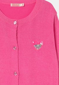 Rosa stickad kofta med rund halsringning, knappstängning och hjärtformad, genomskinlig ficka fylld med paljetter. Glittrig textur genom hela plagget.