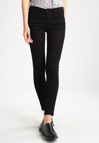 Svarta tight jeans med en slät yta, hög midja och femfickorsdesign, tillsammans med svarta skor med ett dragkedjedetalj.