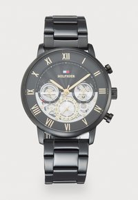 Montre en acier inoxydable noir avec un cadran rond, des accents dorés, un affichage squelettique, des chiffres romains et trois sous-cadrans.
