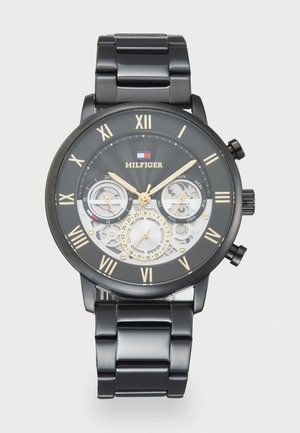 Montre en acier inoxydable noir avec un cadran rond, des accents dorés, un affichage squelettique, des chiffres romains et trois sous-cadrans.