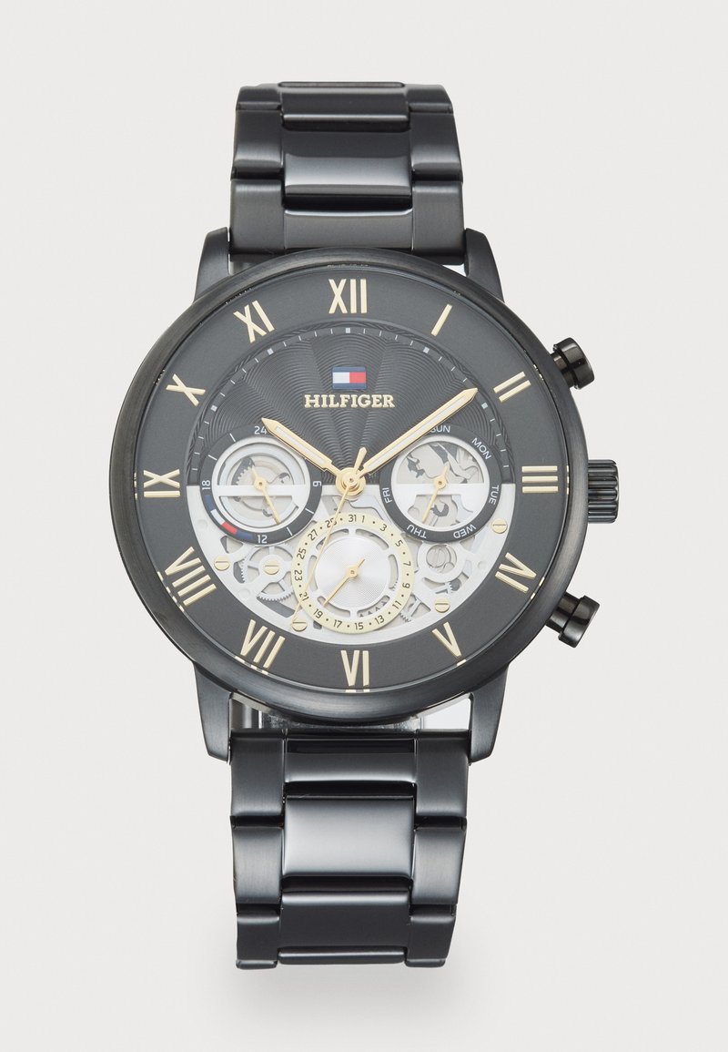 Montre en acier inoxydable noir avec un cadran rond, des accents dorés, un affichage squelettique, des chiffres romains et trois sous-cadrans.