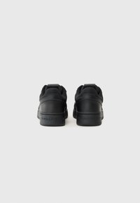 Zwarte sneakers met een glad leren en mesh bovenwerk, gewatteerde kraag en een logo dat op de hak is gedrukt. Platte rubberen zool en een minimalistisch ontwerp.