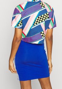 Haut coloré à manches courtes avec des motifs géométriques et des accents à carreaux, associé à une jupe en jersey bleu ajustée avec des bandes latérales.