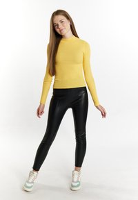 Gelbes geripptes Langarmshirt kombiniert mit glänzenden schwarzen Leggings und mehrfarbigen Sneakern, mit einem figurbetonten Design und nahtloser Textur.