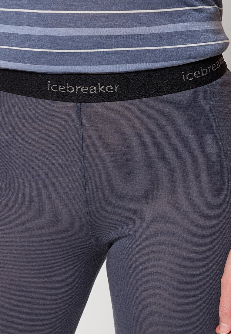 Person, die dunkelgraue Icebreaker-Leggings und ein blau-grau gestreiftes Shirt trägt, mit sichtbarem Logo am Bund.