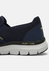 Sötétkék sportcipő hálós felsőrésszel, rugalmas, könnyű talppal és figyelemfelkeltő zöld kiegészítőkkel. Jellemzője a slip-on dizájn, ami megkönnyíti a felvételt.