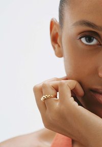 Anillo de oro con tres acentos esféricos de diferentes tamaños. Superficie lisa, diseño simple, llevado en un dedo cerca de una mano.