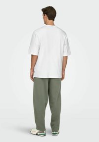 Hvid bomuld t-shirt med korte ærmer, afslappet pasform, kombineret med olivengrønne bukser med afslappet pasform og hvide sneakers med grønne detaljer.