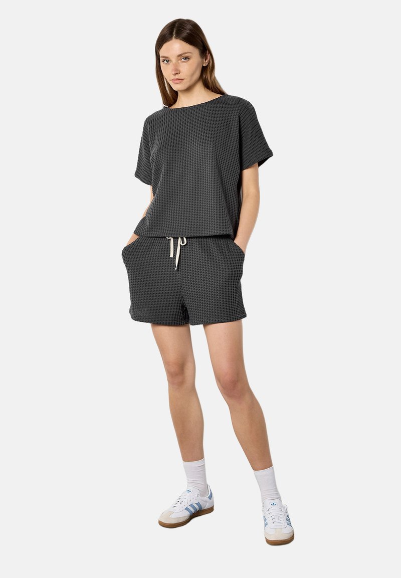 Femme portant un haut à manches courtes texturé gris foncé et un short assorti avec poches, des chaussettes blanches et des baskets blanches à rayures bleues.