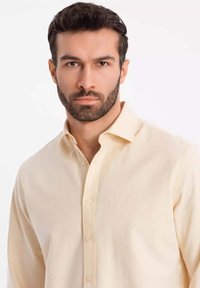 Cremefarbendes Button-up-Hemd aus weichem Stoff. Verfügt über einen klassischen Kragen und lange Ärmel mit geknöpften Manschetten. Minimale Details.