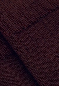 Brunt strikket stof med en ribbet tekstur, der har tætte lodrette linjer og et blødt udseende, foldet for at vise dybde og detaljer.