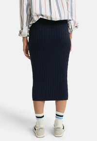 Gonna a matita lavorata a maglia di colore navy con motivo a treccia, abbinata a calzettoni bianchi con strisce blu e nere e scarpe da ginnastica casual.