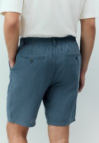 Pantaloni scurți din in albastri pentru bărbați, cu talie elastică, două buzunare la spate și o textură netedă. Scurtați la lungimea genunchiului.