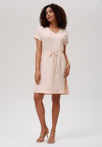 Light pink short-sleeve dress with a V-neck, textured fabric, and a cinched waist. Features a relaxed fit and above-knee length.