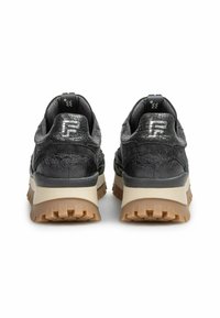 Baskets noires texturées avec une semelle en caoutchouc, présentant une semelle intermédiaire beige, des crampons prononcés et un logo réfléchissant au niveau du talon.
