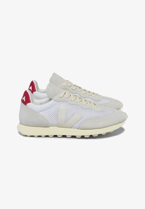 White athletic shoes with grey suede accents, mesh panels, and red heel tabs. Features a textured sole and prominent logo on the side.