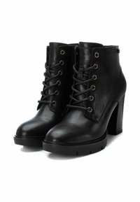 Botas de tobillo de cuero negro con tacón alto. Incluyen ojales de metal, cordones y una suela gruesa. Textura suave con un diseño elegante.