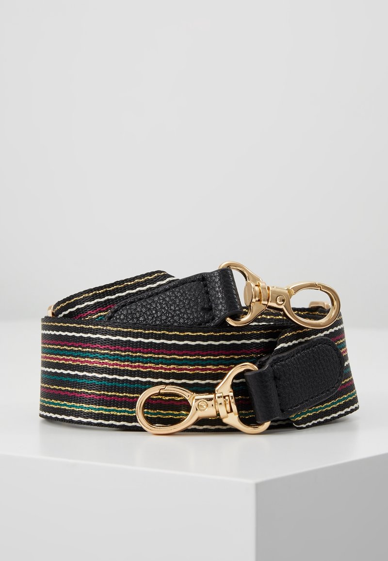 Sangle de sac en tissu rayé coloré avec extrémités en cuir noir et fermoirs pivotants en métal doré, roulée sur une surface blanche.