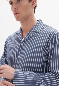 Kék és fehér csíkos ing, gallérral, gombos elülső része van és hosszú ujjú. Az anyag simának tűnik, enyhe textúrával.