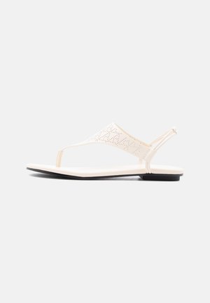 Hvid flad thongsandal med perforeret øvre rem og elastisk bagrem, vist i sideprofil på en ensfarvet baggrund.