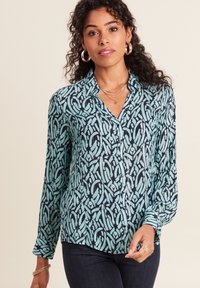 Colloverse blouse in teal en marineblauw met een abstract patroon. Lange mouwen met knoopmanchetten. Lichtgewicht stof met een gladde textuur.