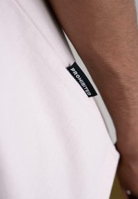 Light pink t-shirt made from cotton, featuring a side label in black with the word "PROHIBITED" in white, smooth texture visible.