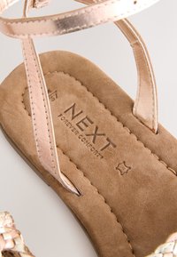 Roségouden sandalen met bandjes en een bruine suède zool, met geperst merklogo "NEXT FOREVER COMFORT" en een gladde textuur.