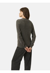 Suéter gris de punto acanalado con cuello redondo, mangas largas y puños ajustados, combinado con pantalones sueltos de un gris oscuro. Detalles de diseño mínimos.