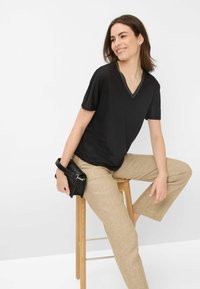 Sort kortærmet V-hals t-shirt med en tekstureret halsudskæring, parret med lysebeige linnedbukser. Modellen holder en sort håndtaske.