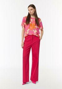 Przezroczysta, kwiatowa bluzka w odcieniach różu i pomarańczy, zestawiona z wysokim stanem, szerokimi spodniami w odcieniu fuksji. Całość dopełniają jaskrawe różowe szpilki.