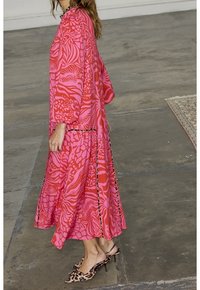 Robe maxi rose à motif avec manches longues, présentant une coupe fluide et un ourlet à bordure contrastée, associée à des talons imprimés léopard.