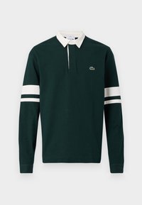 Polo à manches longues vert foncé avec col blanc, deux rayures blanches sur chaque manche, et petit logo crocodile vert sur la poitrine.