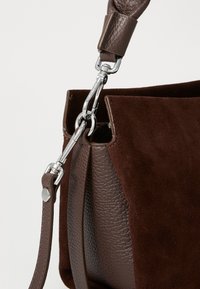 Borsa marrone caratterizzata da una combinazione di pelle liscia e morbida suede, con una chiusura in metallo argentato e una tracolla in pelle regolabile.