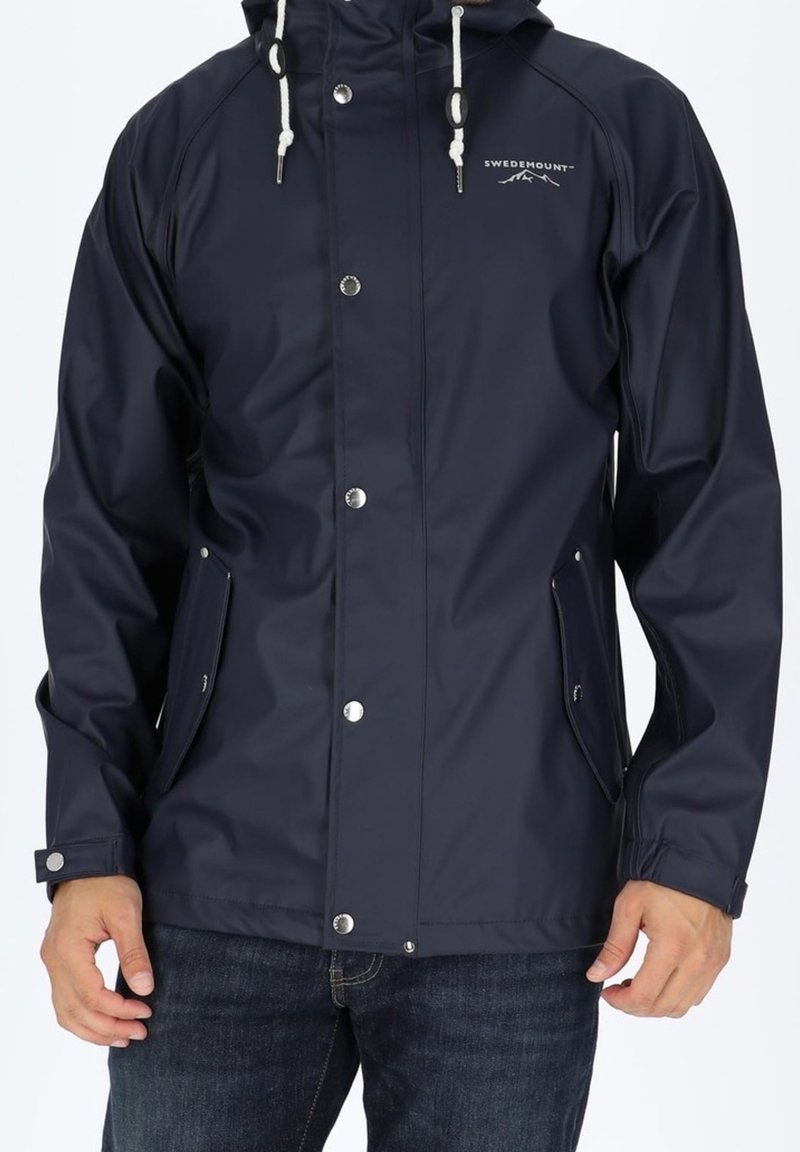 Veste imperméable marine avec capuche, dotée de boutons-pression, de poignets ajustables et de deux poches latérales. Texture lisse avec un logo discret.