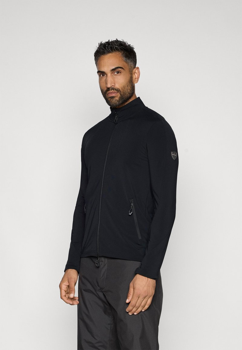 Fekete cipzáras dzseki magas gallérral, két cipzáras oldalzsebbel, sima, rugalmas anyagból készült.