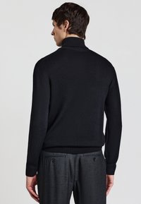 Maglione nero a collo alto realizzato in tessuto a maglia fine, con colletto e polsini in costina, abbinato a pantaloni grigi su misura.