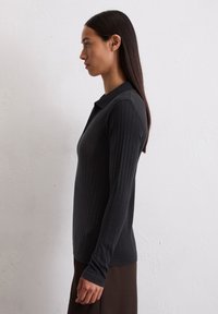 Schwarzes, geripptes Langarmshirt mit Kragen, das überlange Ärmel und eine taillierte Passform hat, kombiniert mit einem dunklen, fließenden Rock.