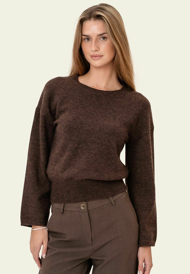 Pull en maille marron avec un col rond, une coupe ample et un ourlet côtelé. Associé à un pantalon marron sur mesure avec un détail de bouton.