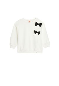 Sudadera blanca de manga larga, con puños y dobladillo acanalados. Presenta dos lazos de tela negra en la parte frontal, en el lado superior izquierdo.