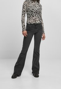 Svarta utsvängda jeans kombinerade med en långärmad topp i zebramönster, med en figurnära silhuett och slät textur. Svarta skor fulländar looken.