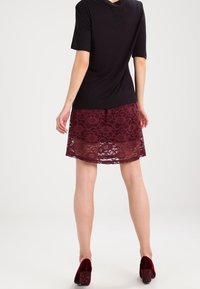 Haut noir à manches courtes associé à une jupe en dentelle bordeaux ornée d'un motif floral, portée avec des talons en velours bordeaux.